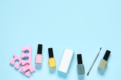 Photo of Nail polishes, toe separators, buffer and cuticle pusher on light blue background, flat lay. Space for text