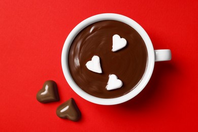 Photo of Cup of hot chocolate with heart shaped marshmallows and tasty candies on red background, flat lay