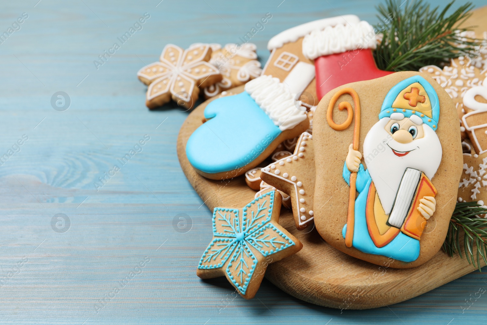 Photo of Tasty gingerbread cookies and fir branches on light blue wooden table, space for text. St. Nicholas Day celebration