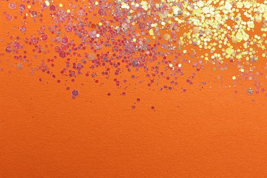 Photo of Shiny bright lilac glitter on orange background, flat lay. Space for text
