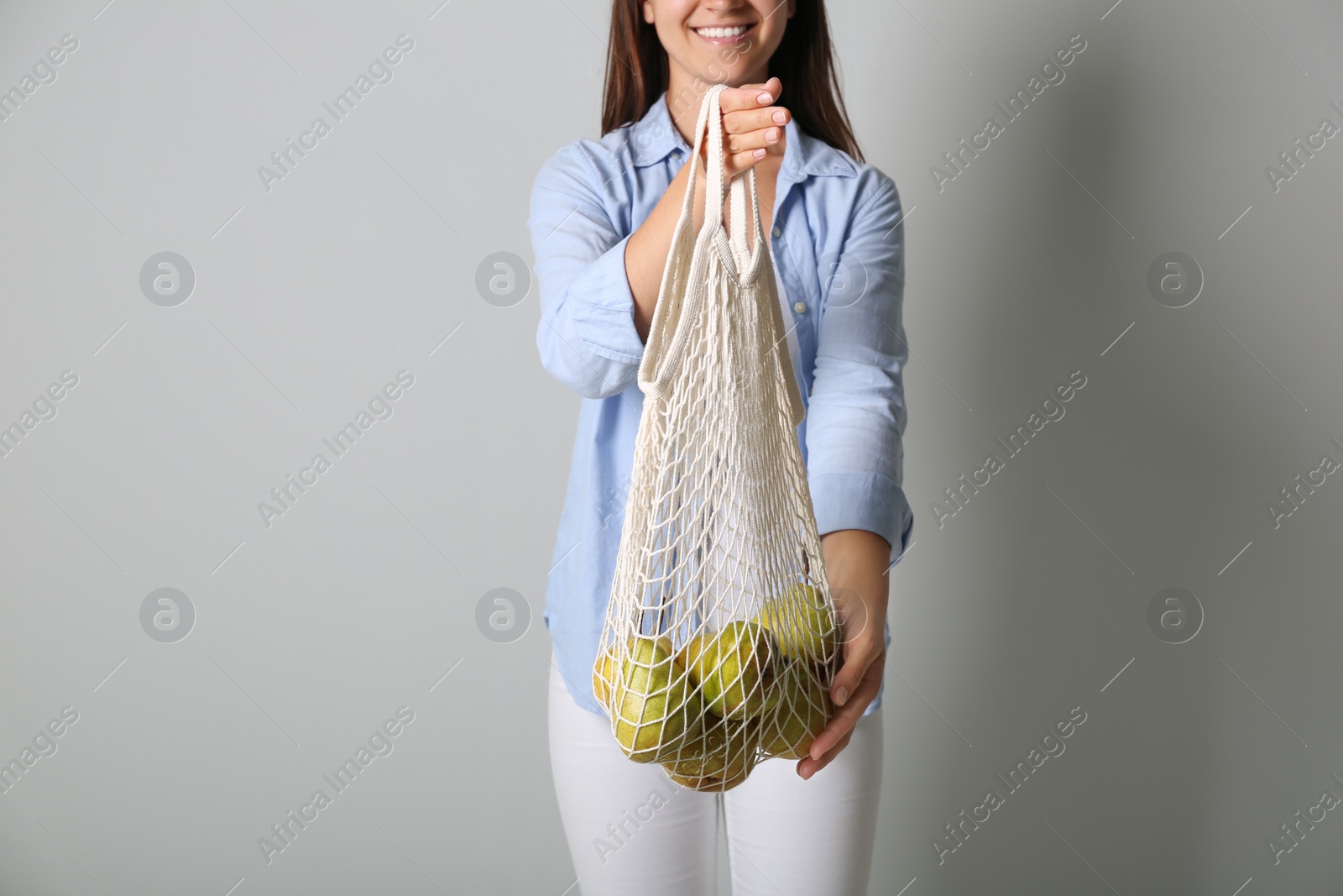 Photo of Woman holding net bag with fresh ripe pears on grey background, closeup