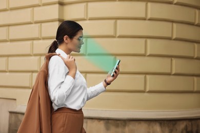 Image of Woman using smartphone with facial recognition system on street. Security application scanning her face for approving owner's identity
