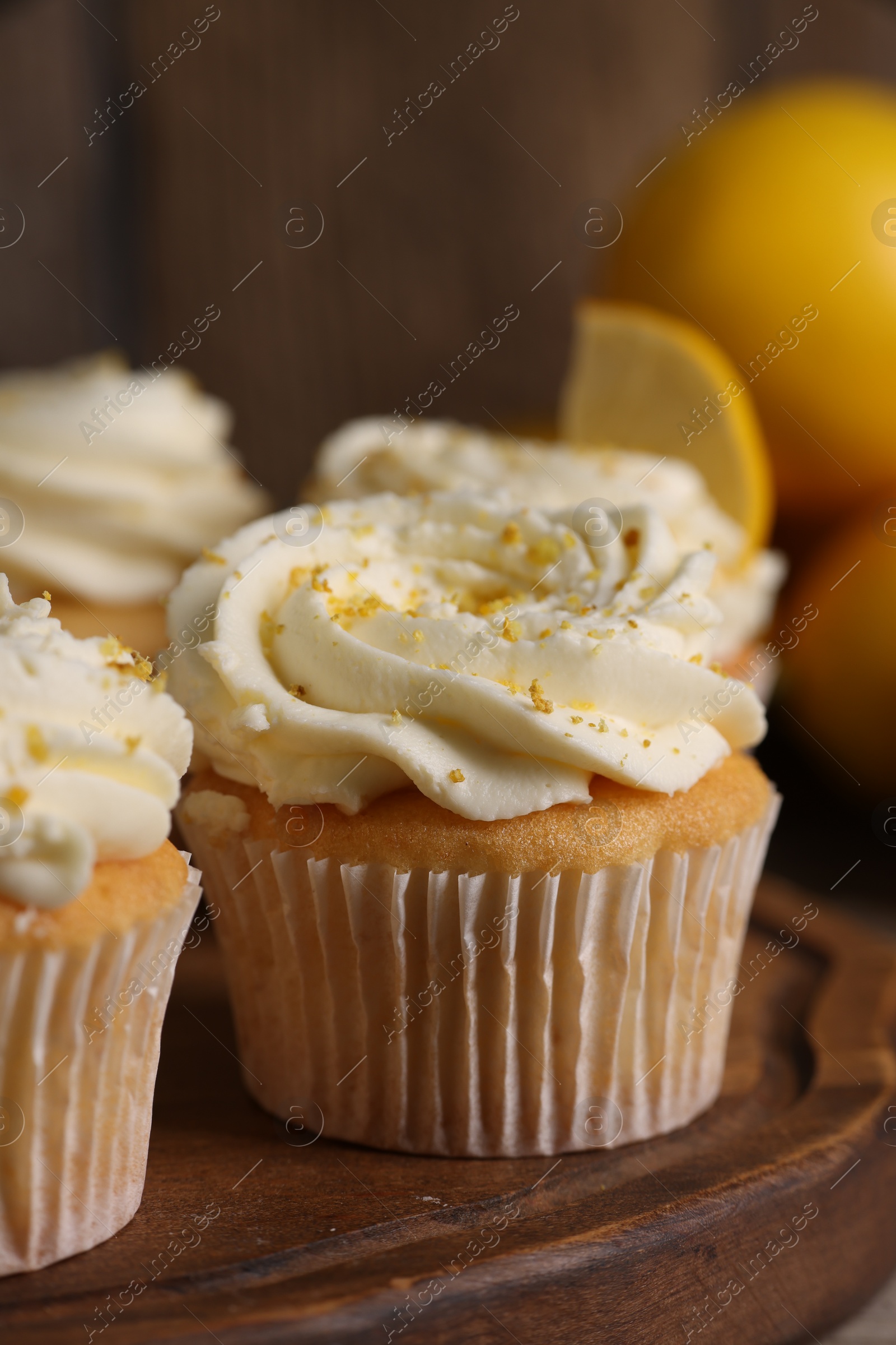 Photo of Delicious cupcakes with white cream and lemon zest on wooden board, closeup