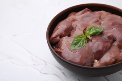 Photo of Bowl with raw chicken liver and basil on white textured table, closeup. Space for text