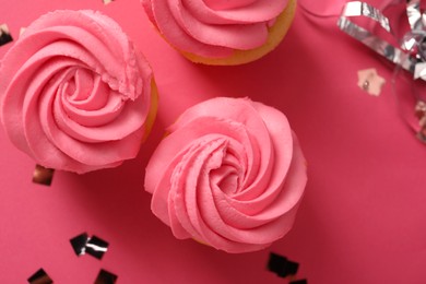 Photo of Delicious cupcakes with bright cream and confetti on pink background, flat lay