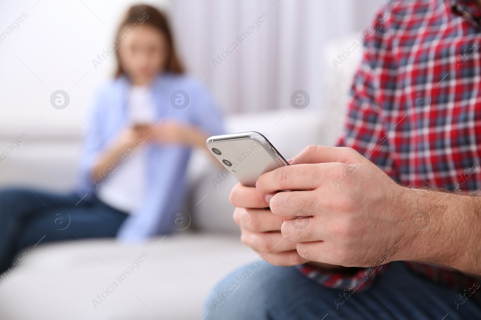 Photo of Man with smartphone ignoring his girlfriend at home, closeup. Relationship problems