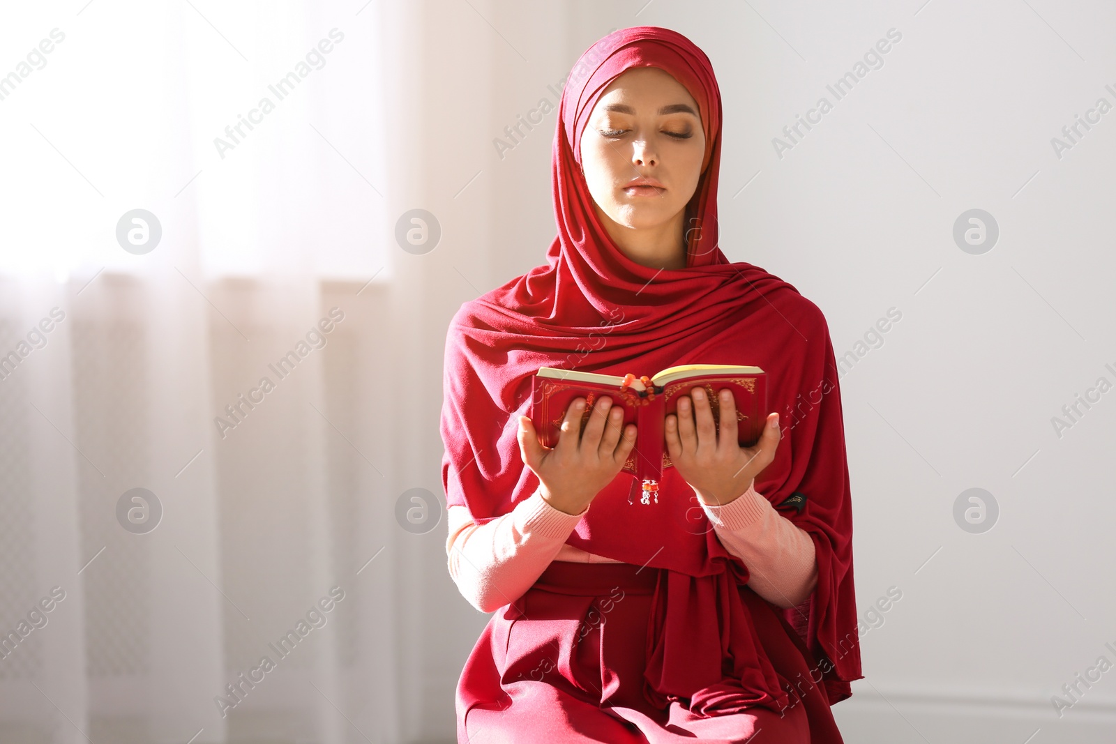 Photo of Muslim woman in hijab reading Koran indoors