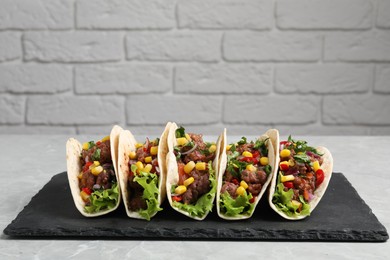 Photo of Delicious tacos with meat and vegetables on light gray marble table against brick wall