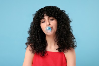 Photo of Beautiful young woman blowing bubble gum on light blue background