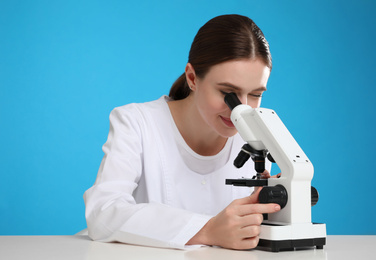 Photo of Scientist using modern microscope at table against blue background. Medical research