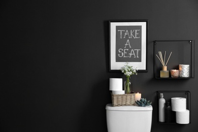 Photo of Decor elements, necessities and toilet bowl near black wall, space for text. Bathroom interior