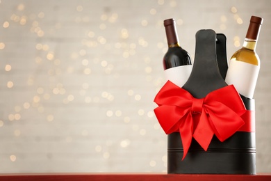 Photo of Bottles of wine in holder with bow against blurred lights. Space for text