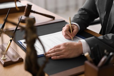 Photo of Notary writing notes at wooden table in office, closeup