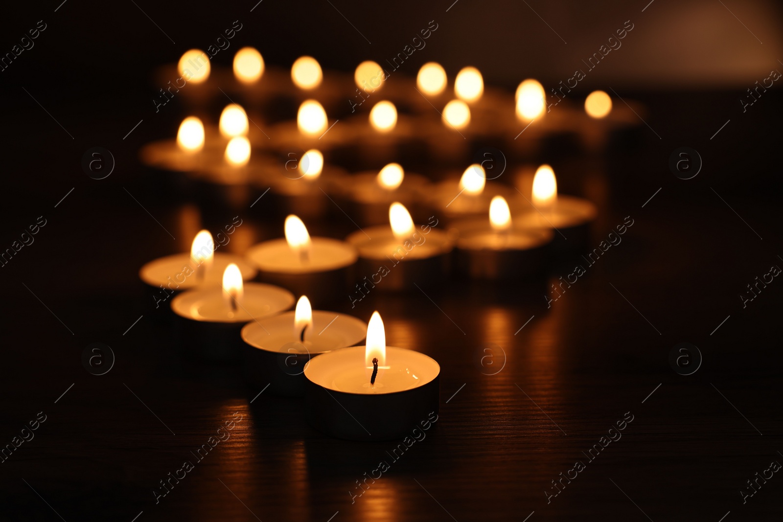 Photo of Burning tealight candles on dark surface, closeup