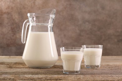 Photo of Jug and glasses of fresh milk on wooden table