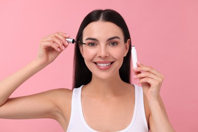 Photo of Beautiful woman applying serum onto her eyelashes on pink background. Cosmetic product