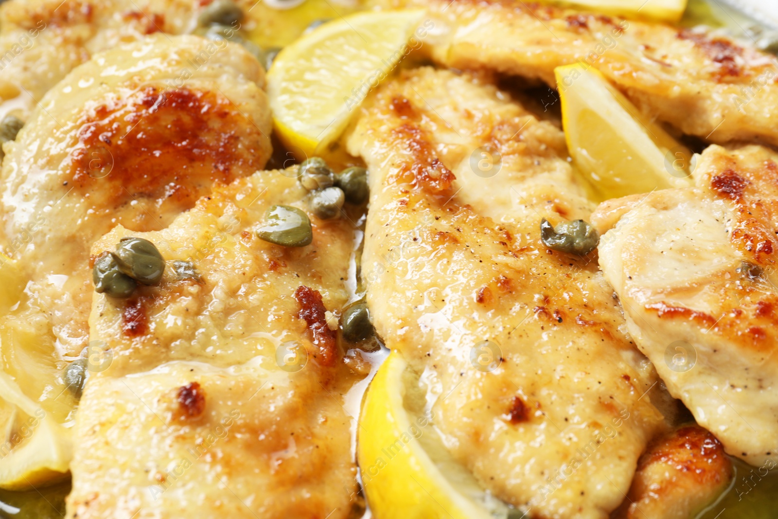 Photo of Delicious chicken piccata with lemons as background, closeup