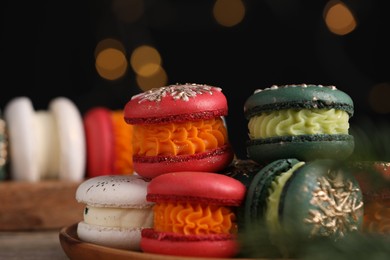 Photo of Beautifully decorated Christmas macarons on table against blurred lights, closeup
