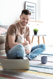 Young man with cute cat and laptop at home