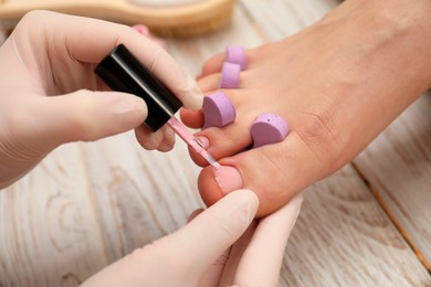 Professional pedicurist painting client`s toenails with polish in beauty salon, closeup