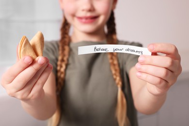 Photo of Girl holding tasty fortune cookie and prediction indoors, closeup