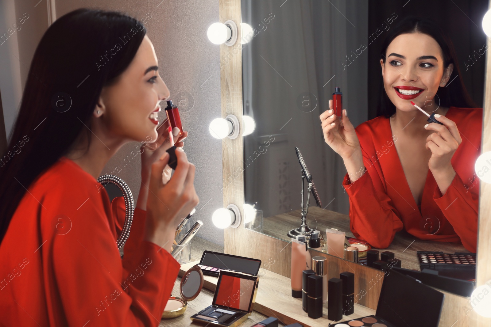 Photo of Beautiful woman applying makeup near mirror in room