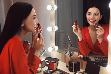 Photo of Beautiful woman applying makeup near mirror in room