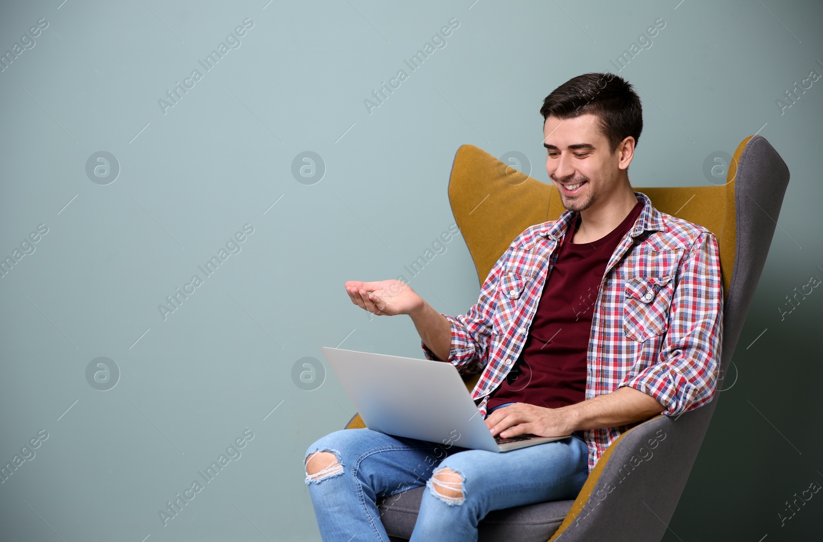 Photo of Young blogger with laptop sitting in armchair against color wall
