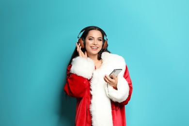 Young woman in Santa costume listening to Christmas music on color background