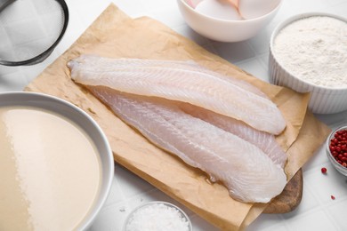 Different ingredients for batter and raw fish fillet on white tiled table