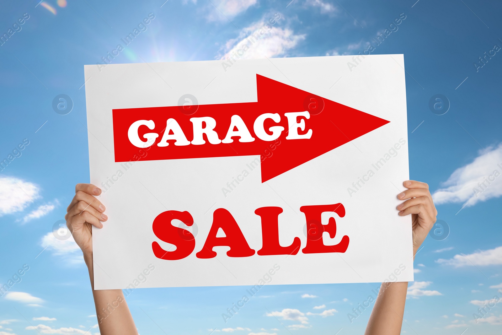 Image of Woman holding sign with text GARAGE SALE against blue sky