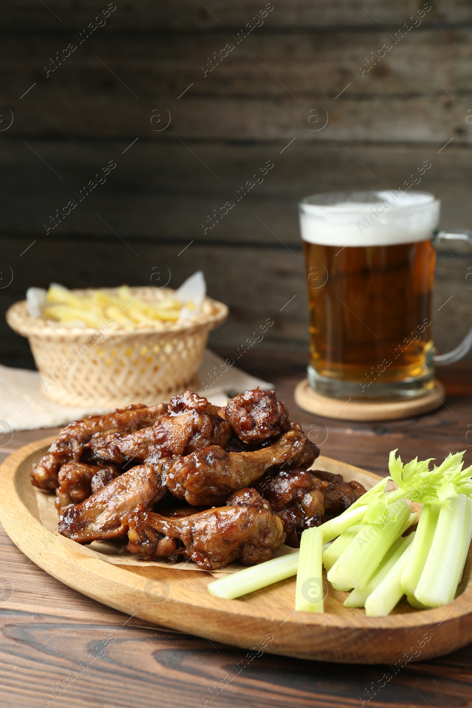 Photo of Delicious chicken wings, celery, beer and french fries on wooden table