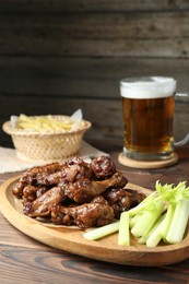 Photo of Delicious chicken wings, celery, beer and french fries on wooden table