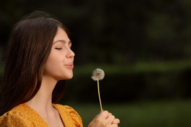 Teenage girl blowing dandelion in park. Space for text