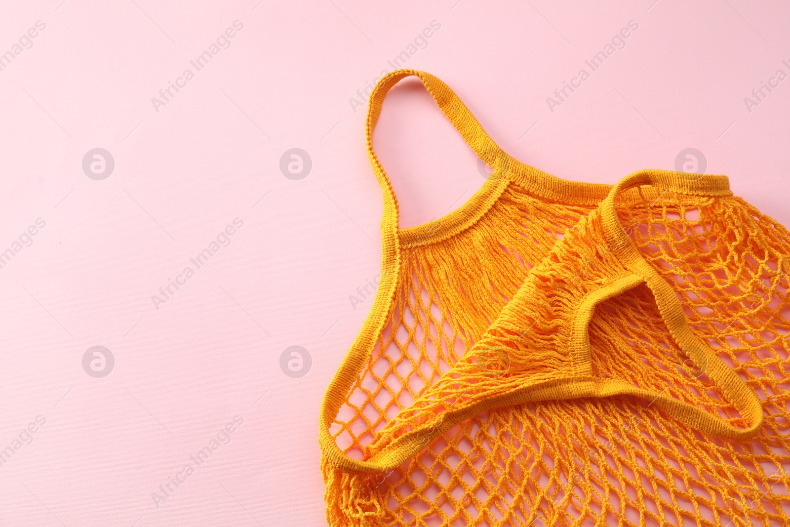 Photo of Orange string bag on pink background, top view. Space for text