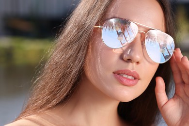 Image of Beautiful woman in sunglasses on sunny day outdoors. Sky, palm tree and observation wheel reflecting in lenses