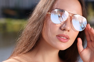 Beautiful woman in sunglasses on sunny day outdoors. Sky, palm tree and observation wheel reflecting in lenses