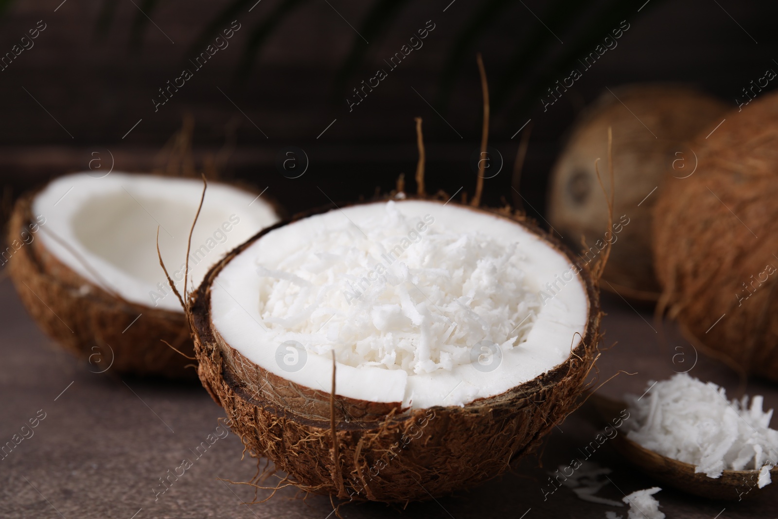 Photo of Coconut flakes in nut shell and spoon on brown table