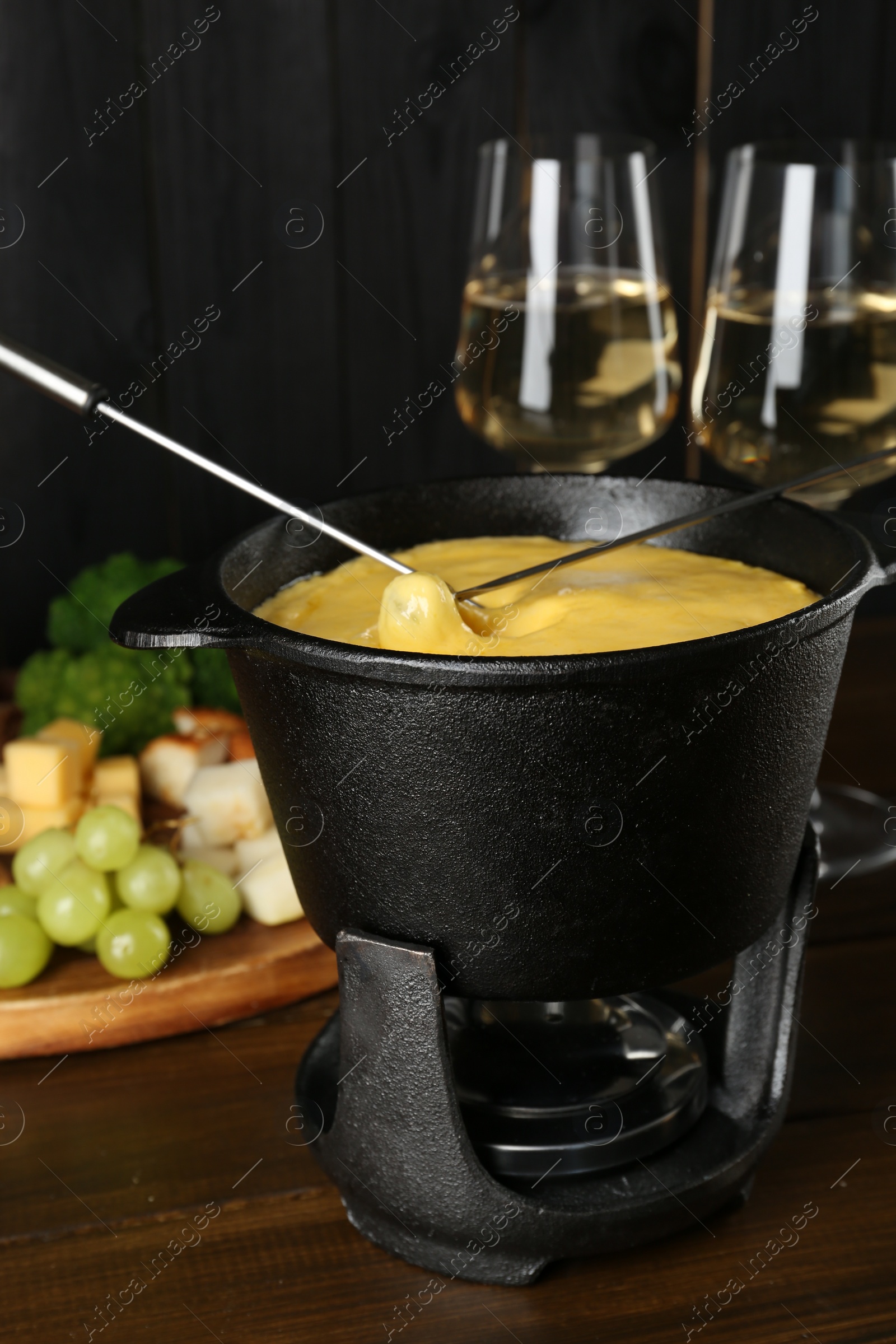 Photo of Dipping different products into fondue pot with melted cheese on wooden table