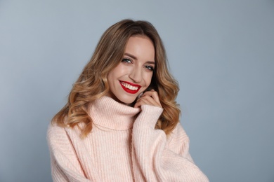 Photo of Happy young woman wearing warm sweater on grey background. Christmas celebration