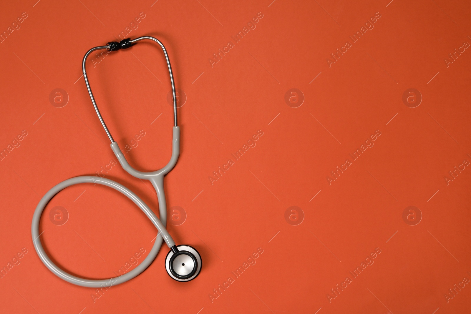 Photo of Stethoscope on crimson background, top view. Space for text