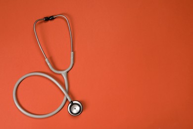 Photo of Stethoscope on crimson background, top view. Space for text