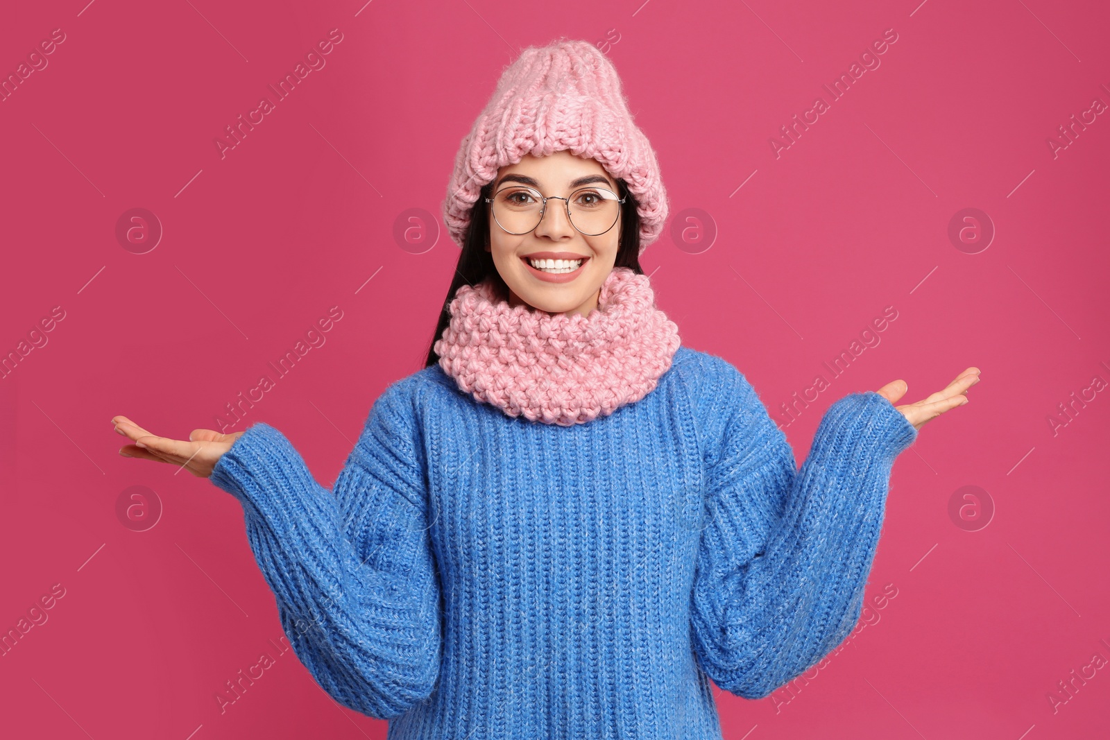 Photo of Young woman wearing warm sweater, snood and hat on crimson background. Winter season