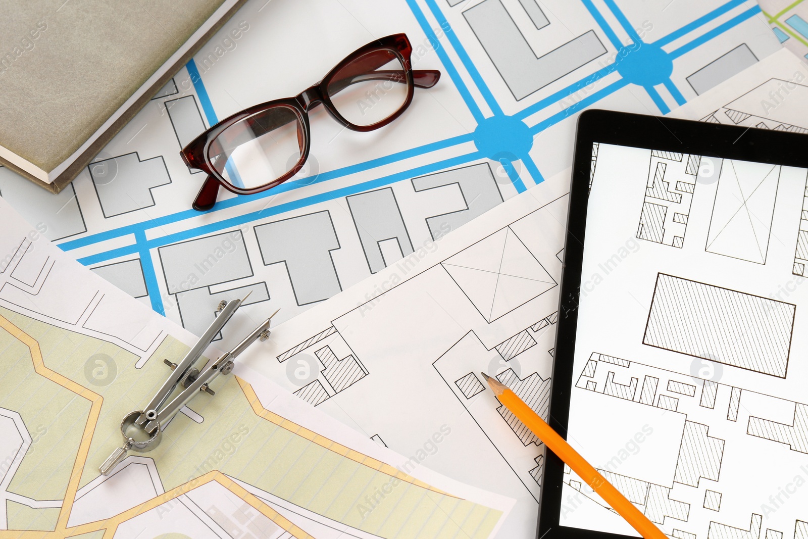 Photo of Office stationery, eyeglasses and tablet on cadastral maps of territory with buildings, flat lay