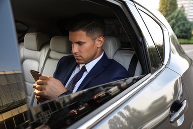 Photo of Handsome man with smartphone on backseat of modern car