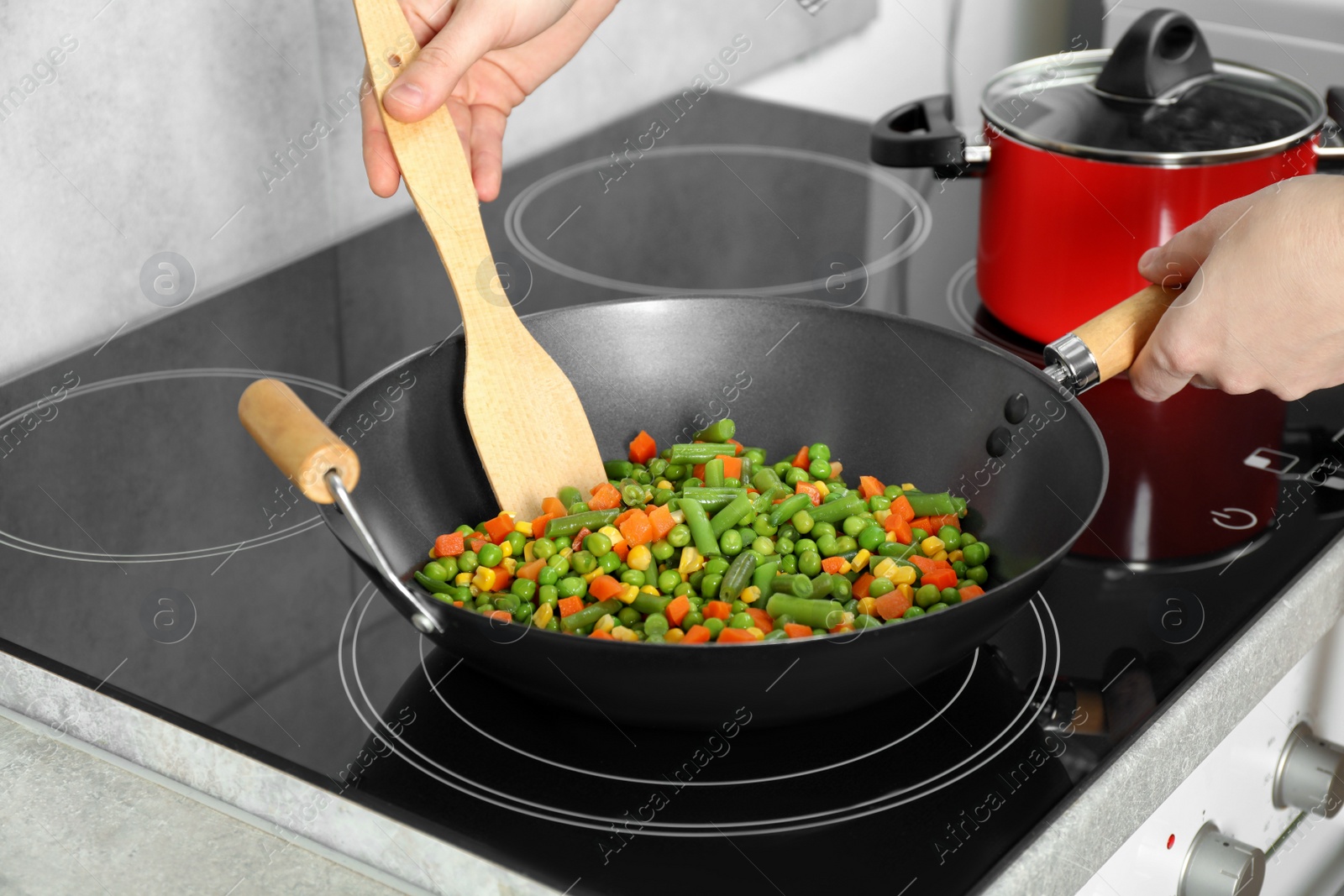 Photo of Woman cooking tasty vegetable mix in wok pan at home, closeup