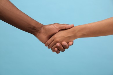 Photo of Woman and African American man shaking hands on light blue background, closeup