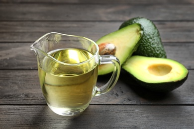 Photo of Jug of natural oil and avocados on wooden background