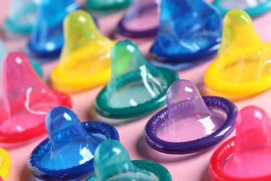 Colorful condoms on pink background, closeup view