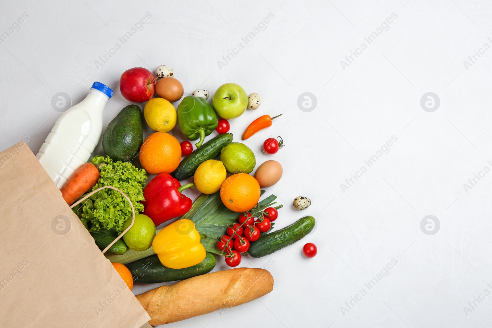 Photo of Flat lay composition with overturned paper bag and groceries on white table. Space for text